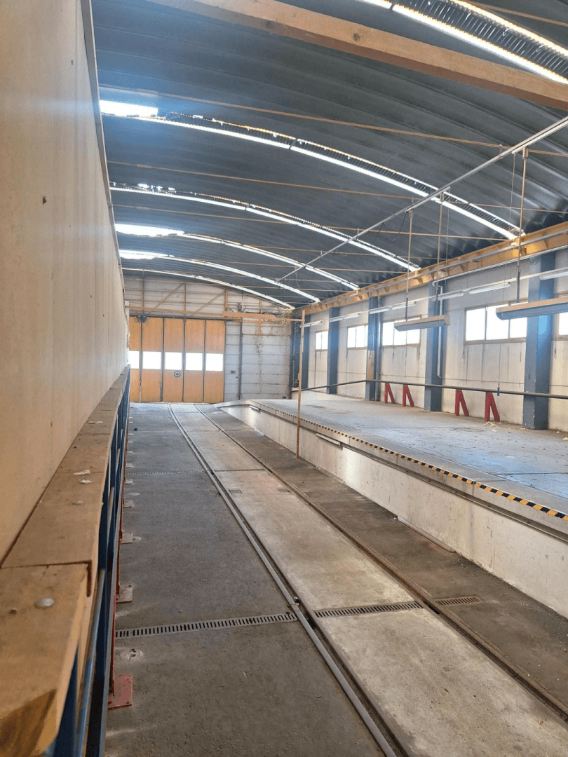 Vertikale Ansicht einer Industriehalle mit Inspektionsgruben, Betonboden und einem großen gelben Rolltor.