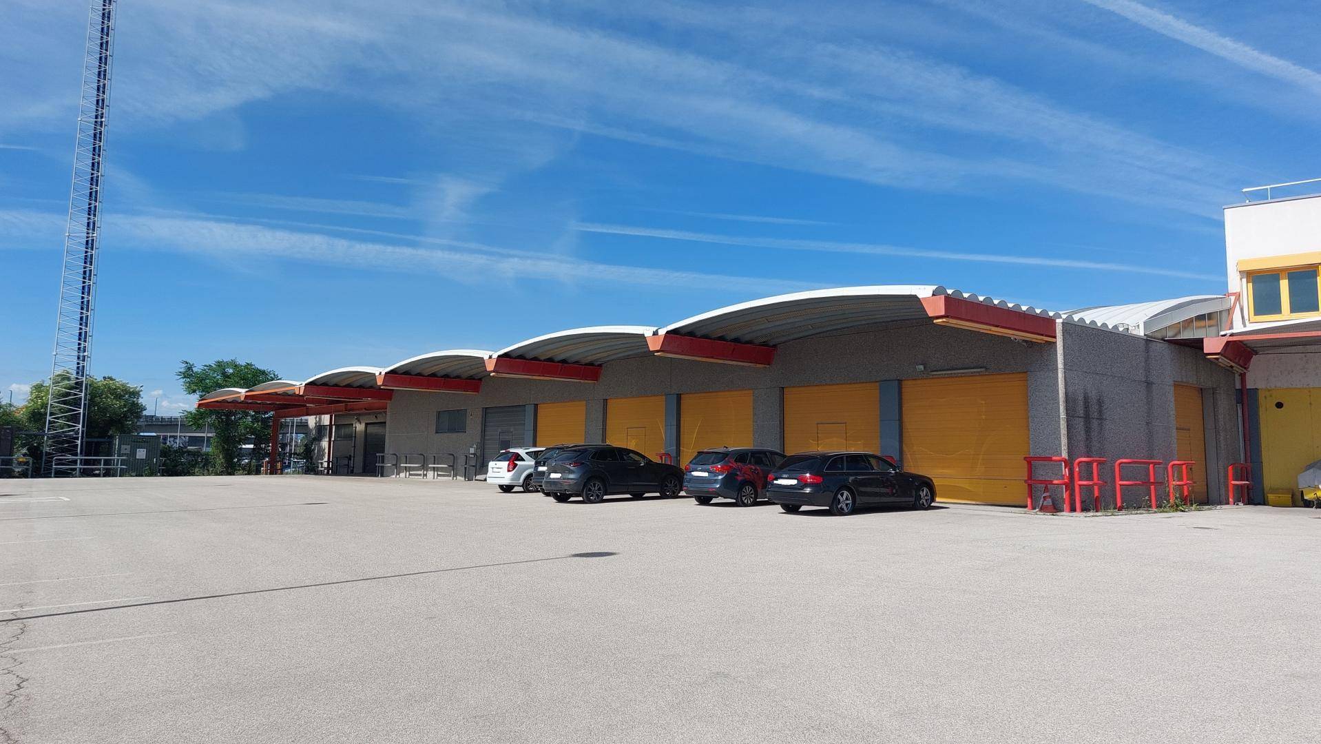 Außenansicht einer Industriehalle mit mehreren gelben Garagentoren und davor geparkten Autos.