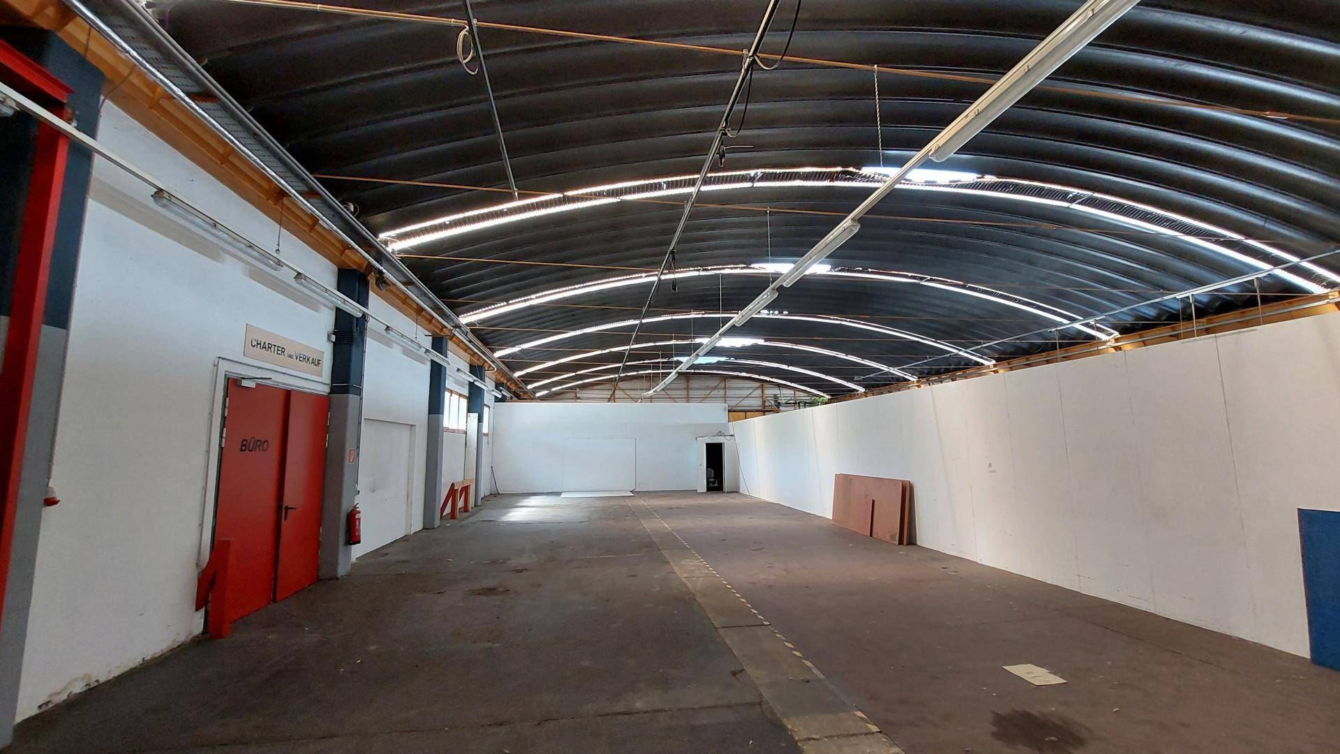 Weitläufiger Innenraum einer Industriehalle mit hohen Decken, Betonboden und viel natürlichem Licht.