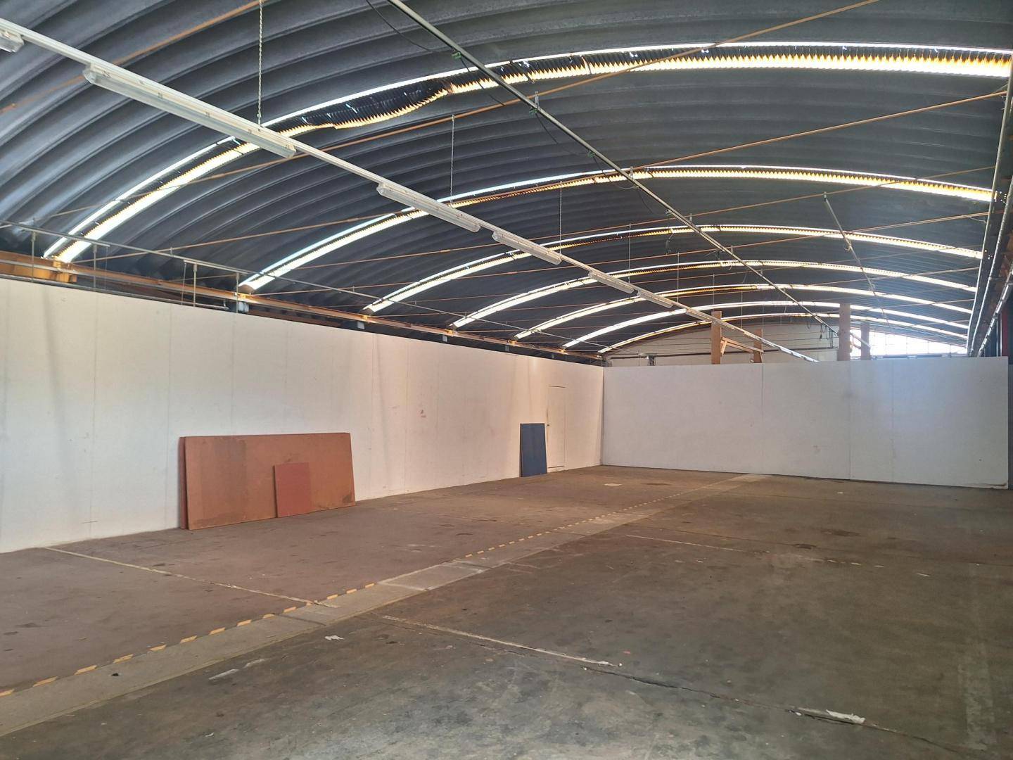 Heller, offener Bereich einer Industriehalle mit weißen Wänden, Betonboden und gewölbtem Dach.