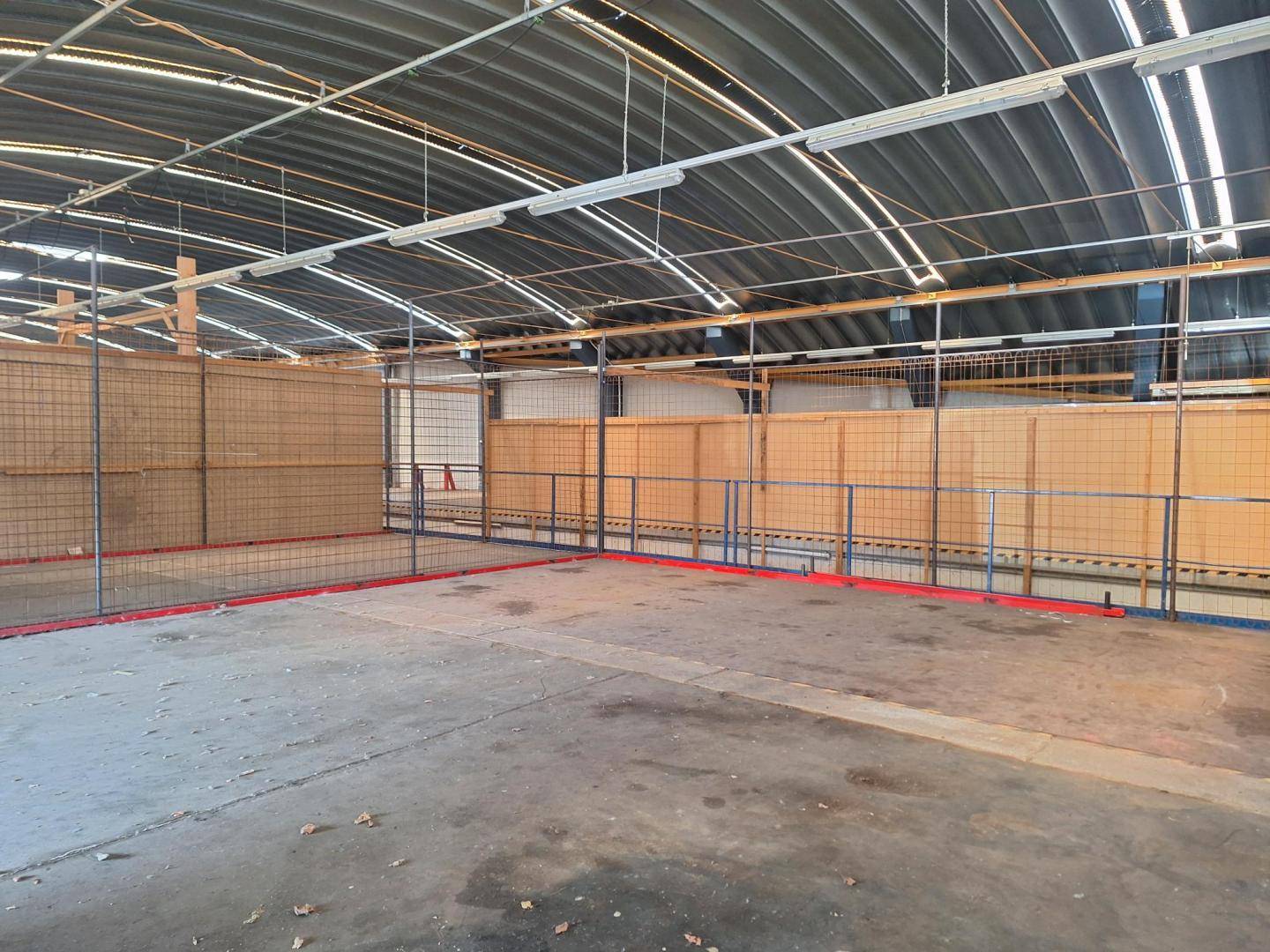 Innenbereich einer Industriehalle mit Metallgitterabtrennungen, Betonboden und gewölbtem Dach.