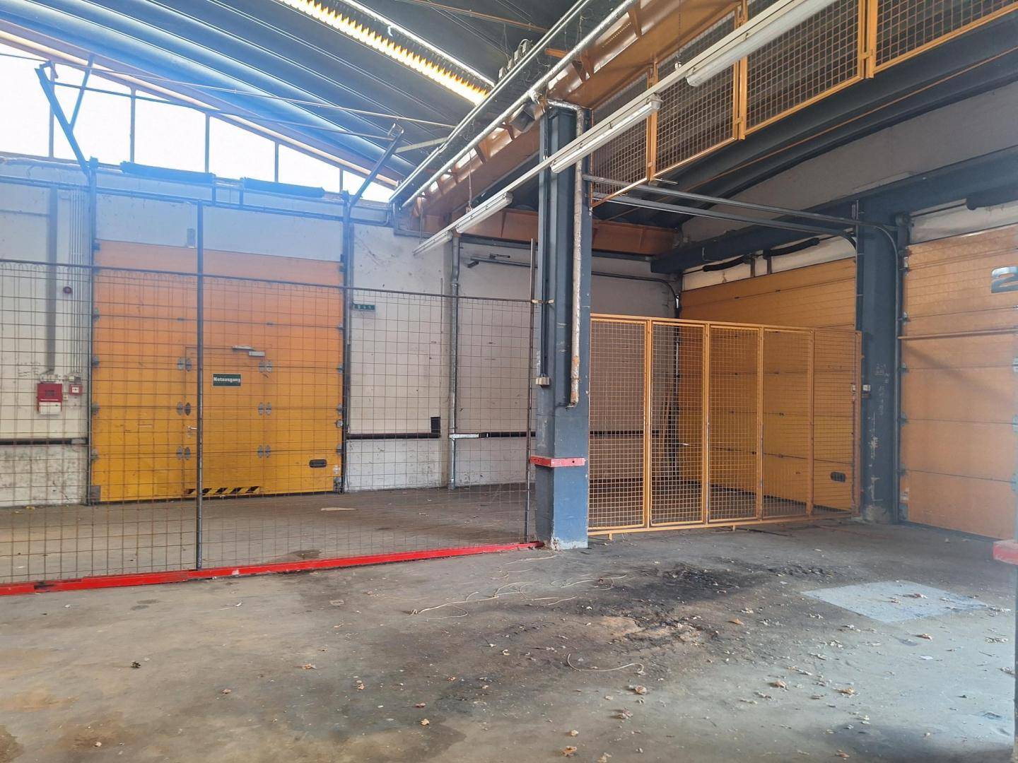 Bereich einer Industriehalle mit gelben Metallgitterkäfigen, großen Rolltoren und Betonboden.