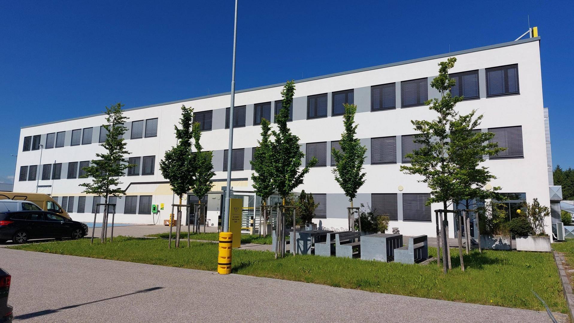 Helles Geschäftsgebäude mit weißer Fassade, zahlreichen Fenstern und Grünflächen im Vordergrund unter klarem Himmel.