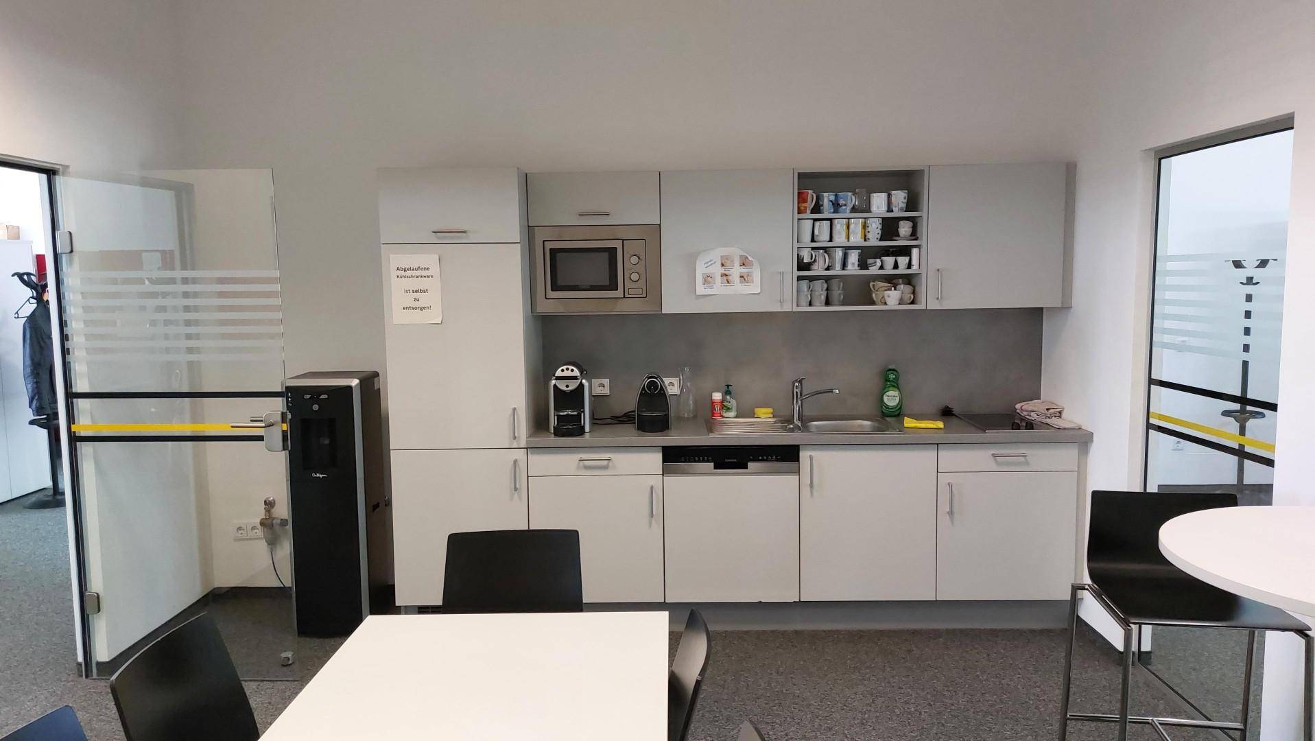 Kleine, funktionale Teeküche mit weißen Schränken, Mikrowelle und Kaffeemaschinen für Mitarbeiterpausen.