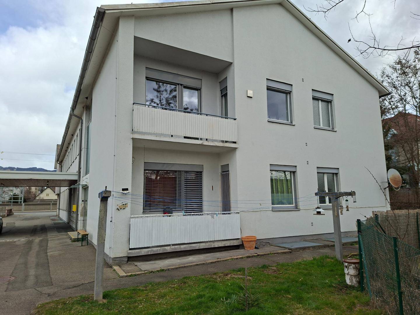 Mehrfamilienhaus mit weißer Fassade, Balkonen und einem kleinen Gartenbereich im Vordergrund.