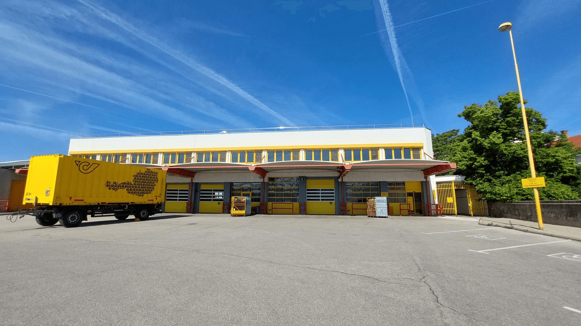 Ansicht der Laderampen und Garagentore eines Gewerbegebäudes mit einem gelben Lastwagenanhänger davor.