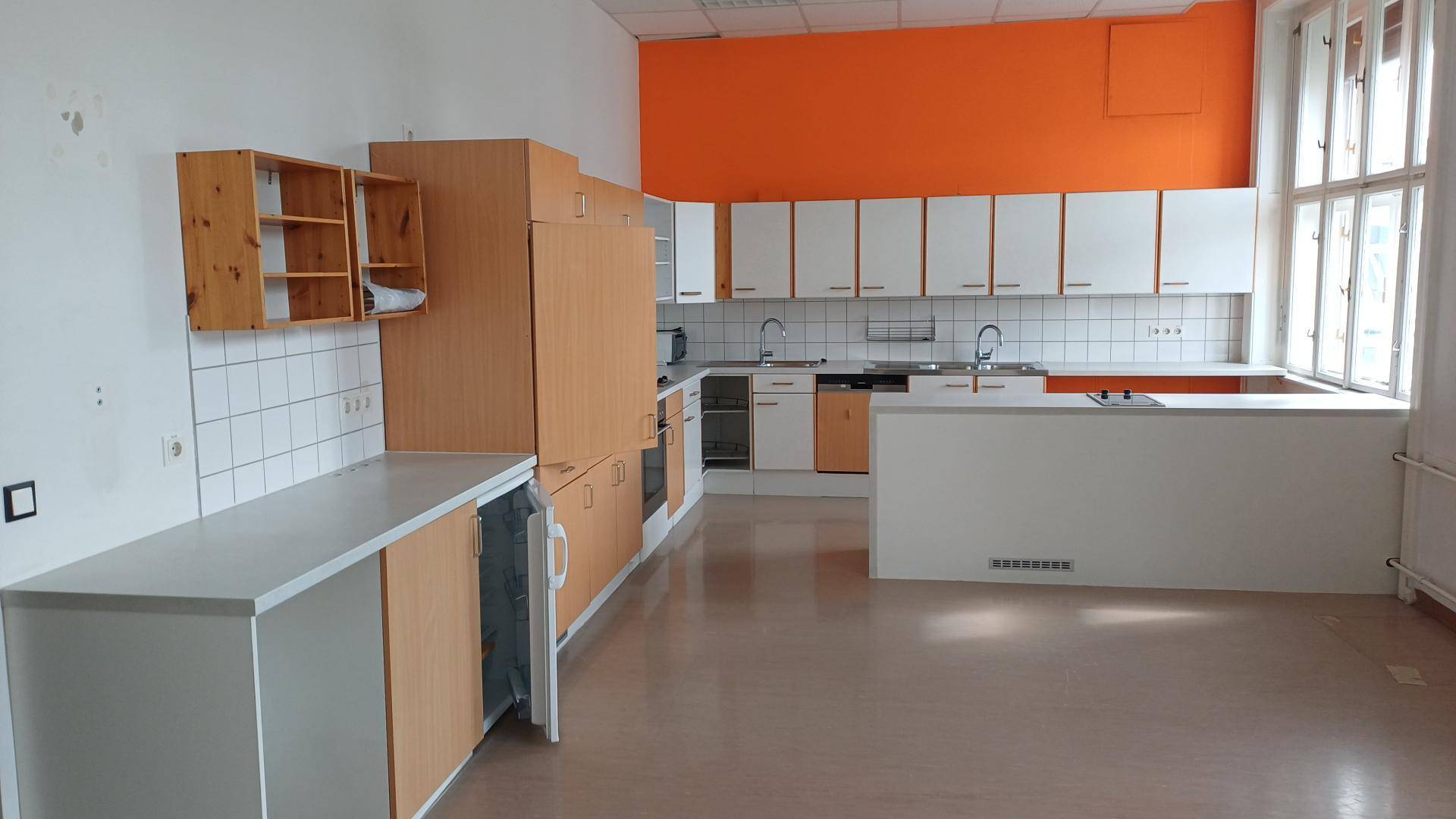 Geräumige Küche mit orangefarbener Akzentwand, weißen und holzfarbenen Schränken und Fliesen.