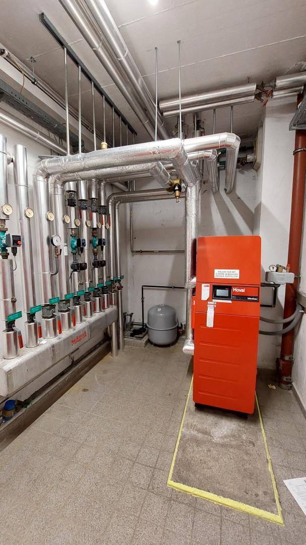 Heizungsraum mit umfangreicher Rohrinstallation und einem großen roten Heizkessel.