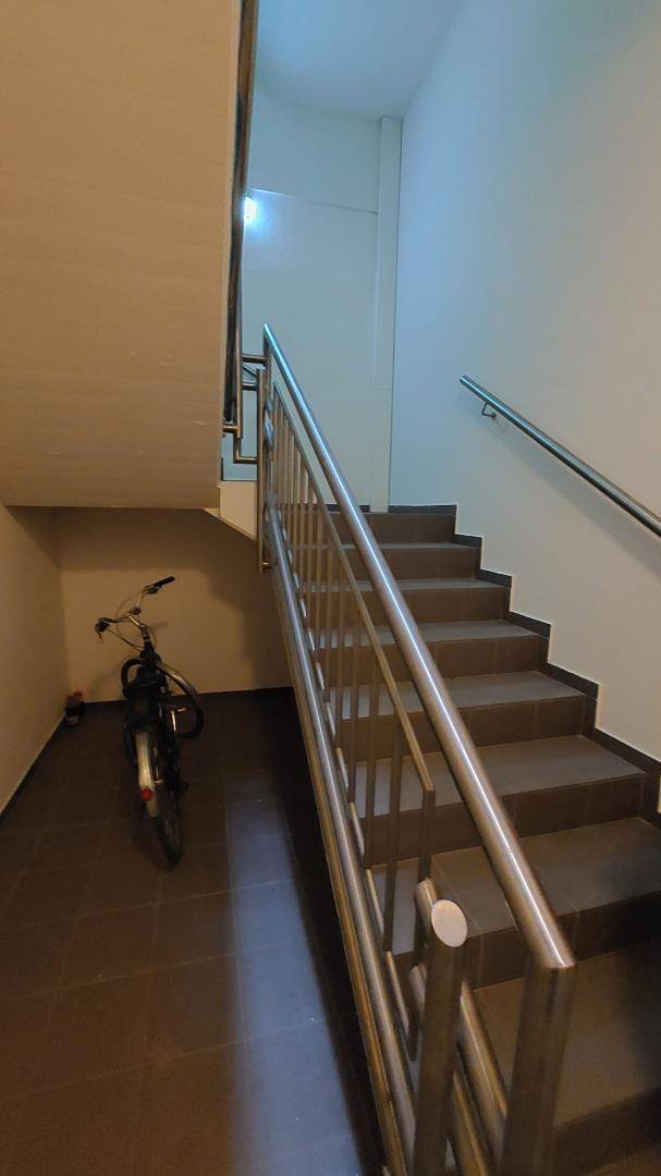 Treppenhaus mit dunklen Fliesenstufen und modernem Metallgeländer, ein Fahrrad steht im unteren Bereich.