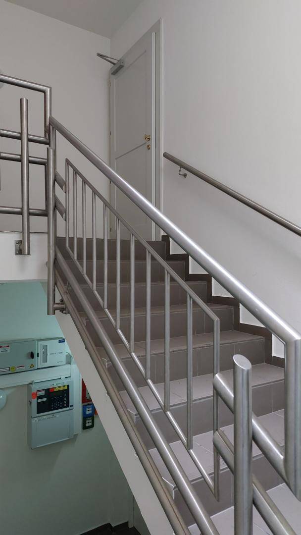 Helles Treppenhaus mit gefliesten Stufen und modernem Metallgeländer, das nach oben führt.