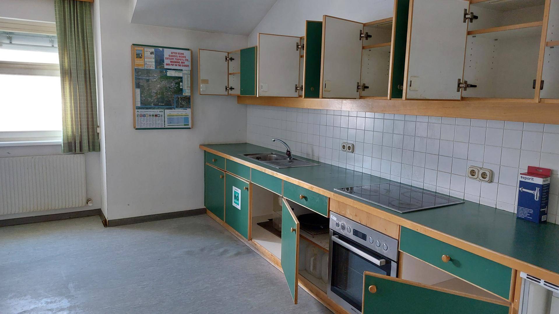 Küche mit grünen Unterschränken, weißen Oberschränken und integriertem Kochfeld und Backofen.
