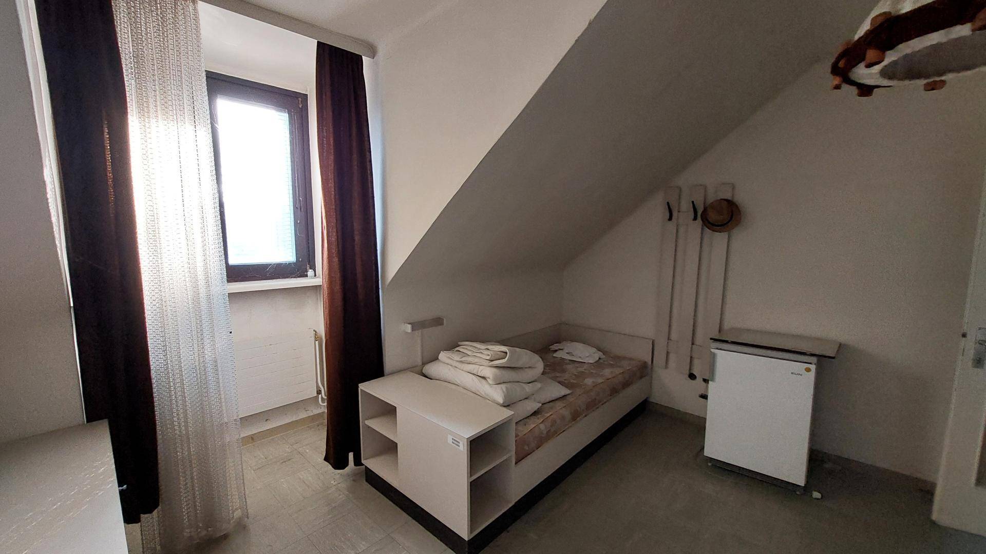 Gemütliches Schlafzimmer im Dachgeschoss mit Einzelbett, kleinem Kühlschrank und schrägen Wänden.