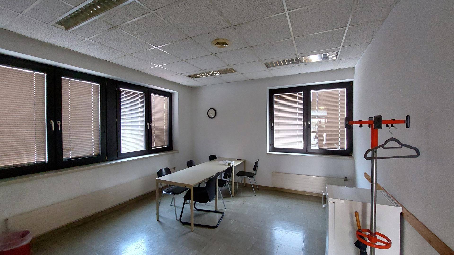Helles Büro oder Besprechungszimmer mit Tisch, Stühlen und Jalousien an den Fenstern.
