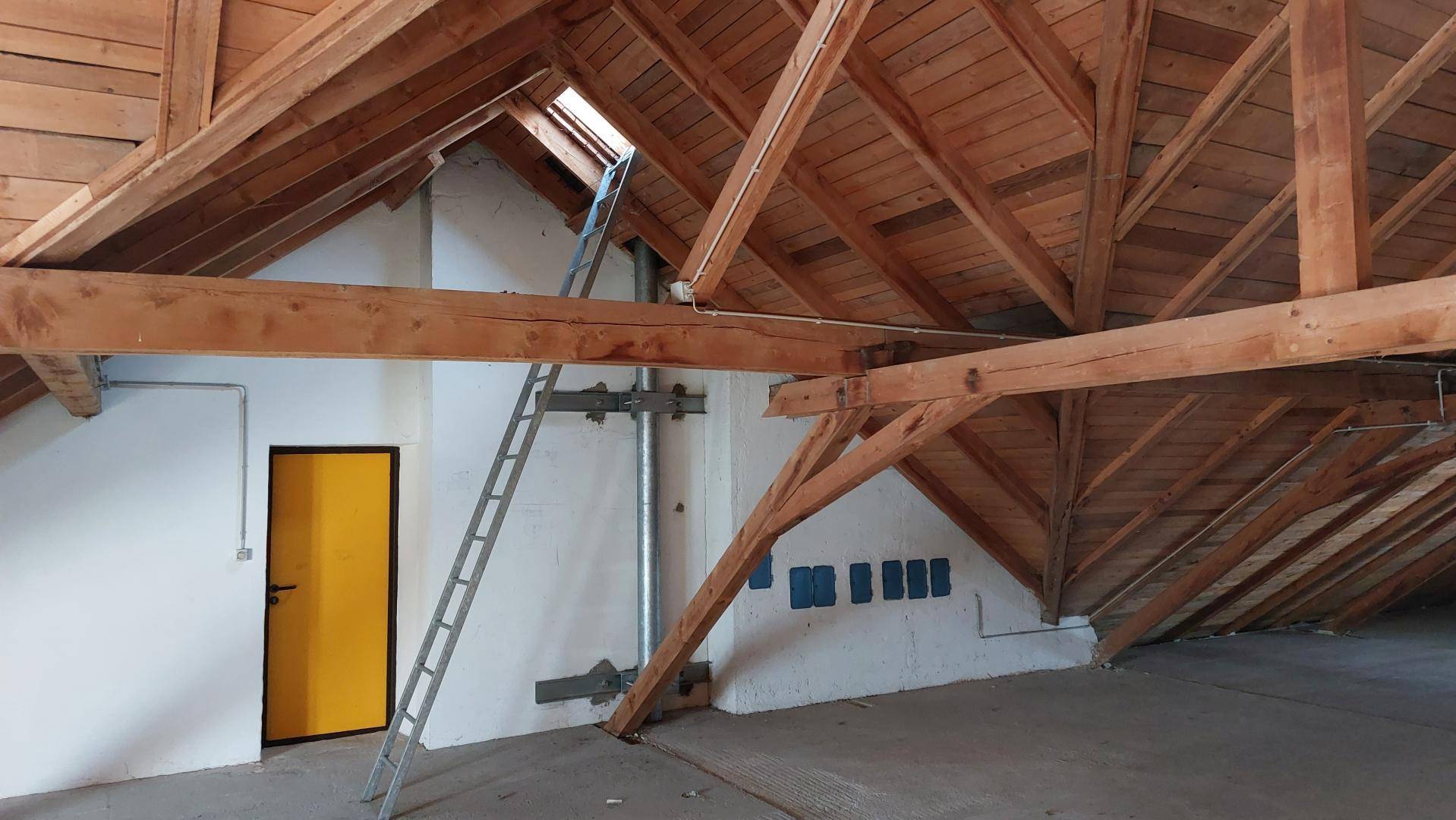 Unausgebauter Dachboden mit sichtbaren Holzbalken, Dachschrägen und einem Dachfenster für Tageslicht.