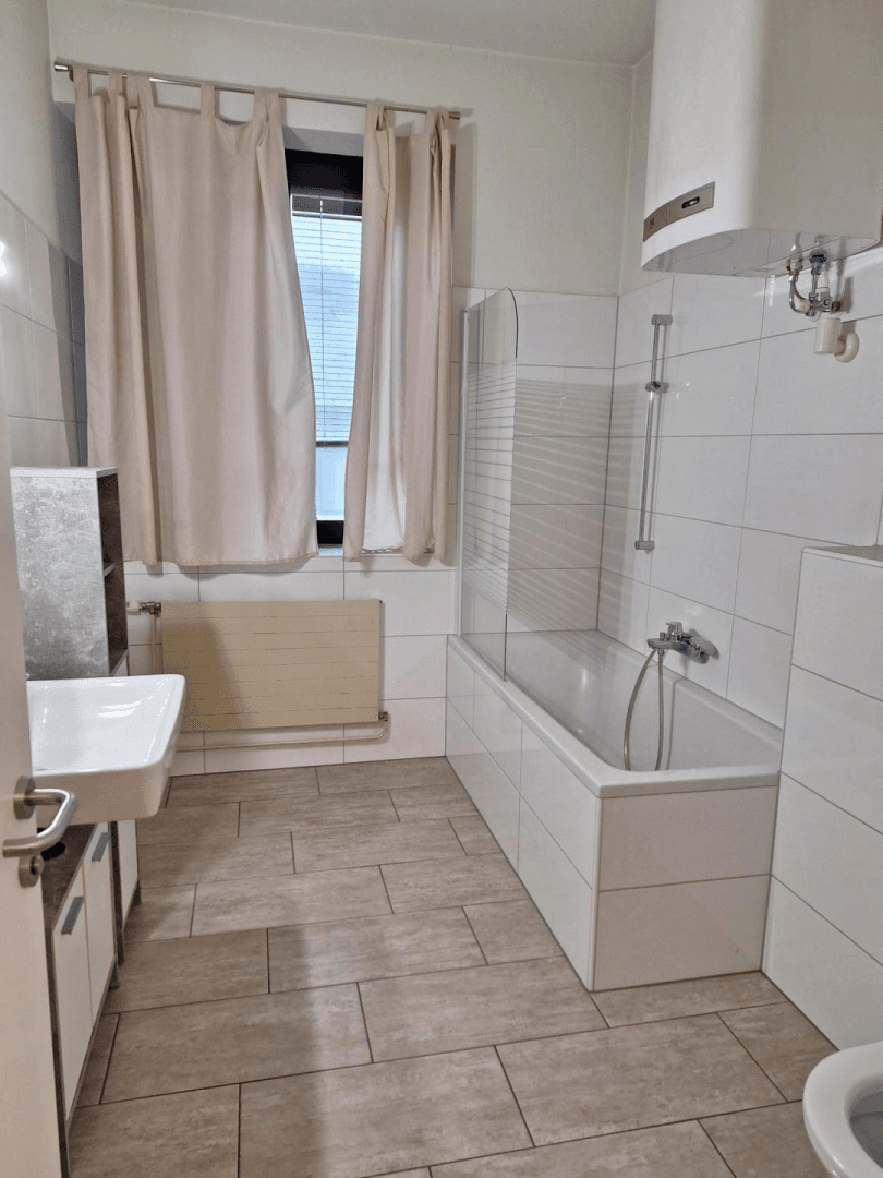 Helles Badezimmer mit Badewanne, Dusche, Waschbecken, Fliesen und einem Fenster für natürliche Belüftung.