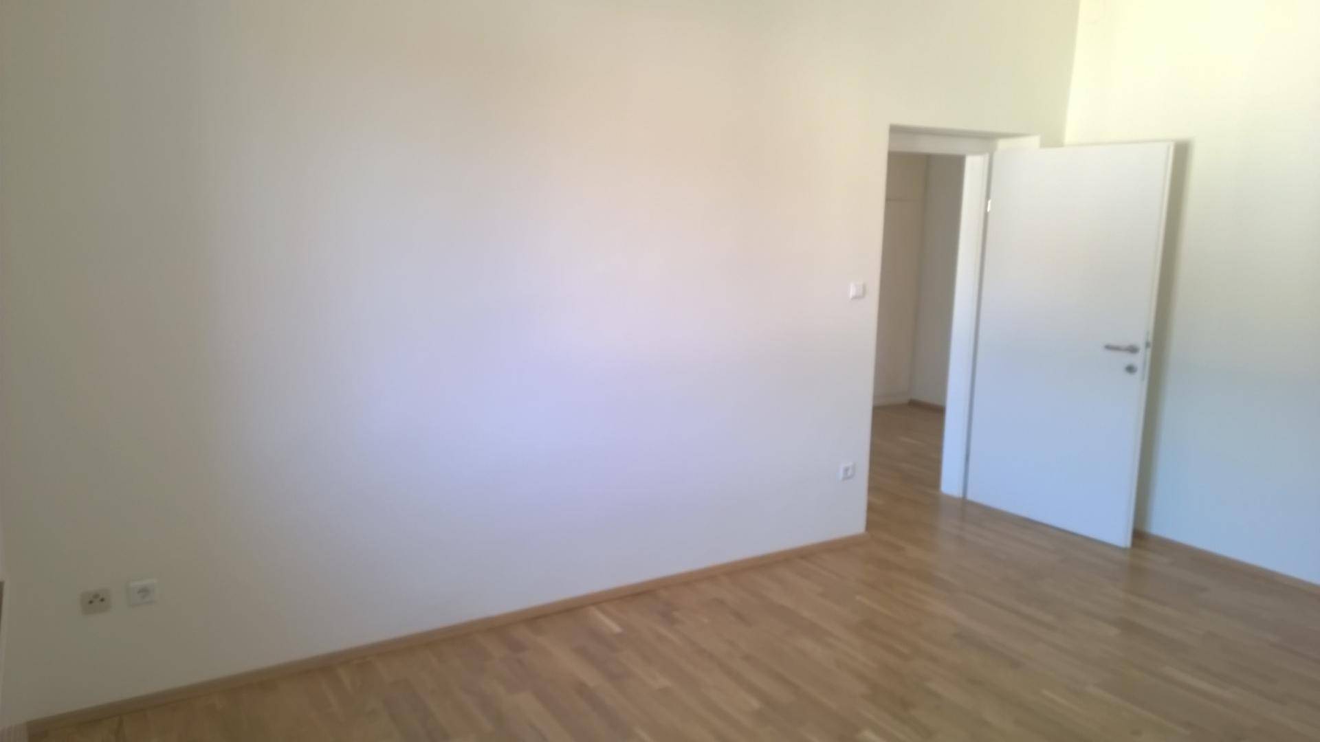 Heller, leerer Raum mit Parkettboden und weißen Wänden, der zu einem weiteren Zimmer führt.