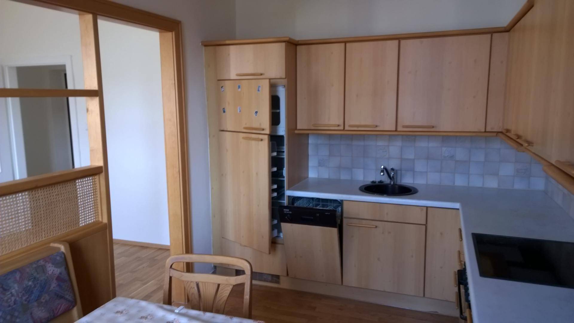 Funktionale Küche mit hellen Holzschränken, Spüle, integrierten Geräten und einem Essbereich.