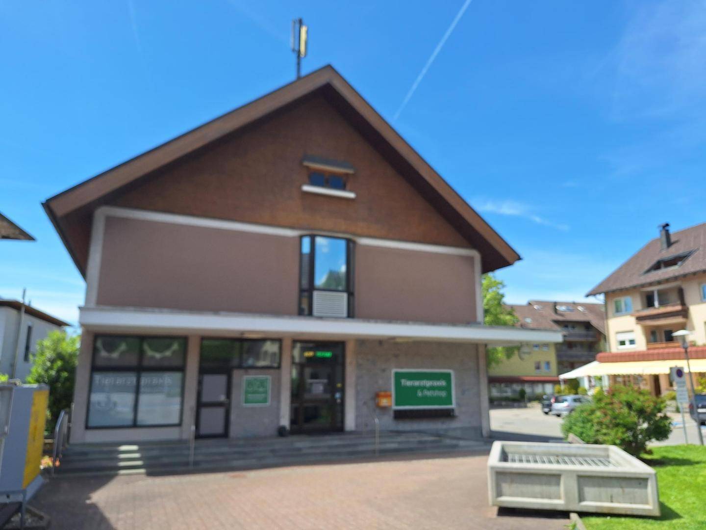 Ansicht des Gebäudes mit brauner Fassade, Giebeldach und klarem blauen Himmel.