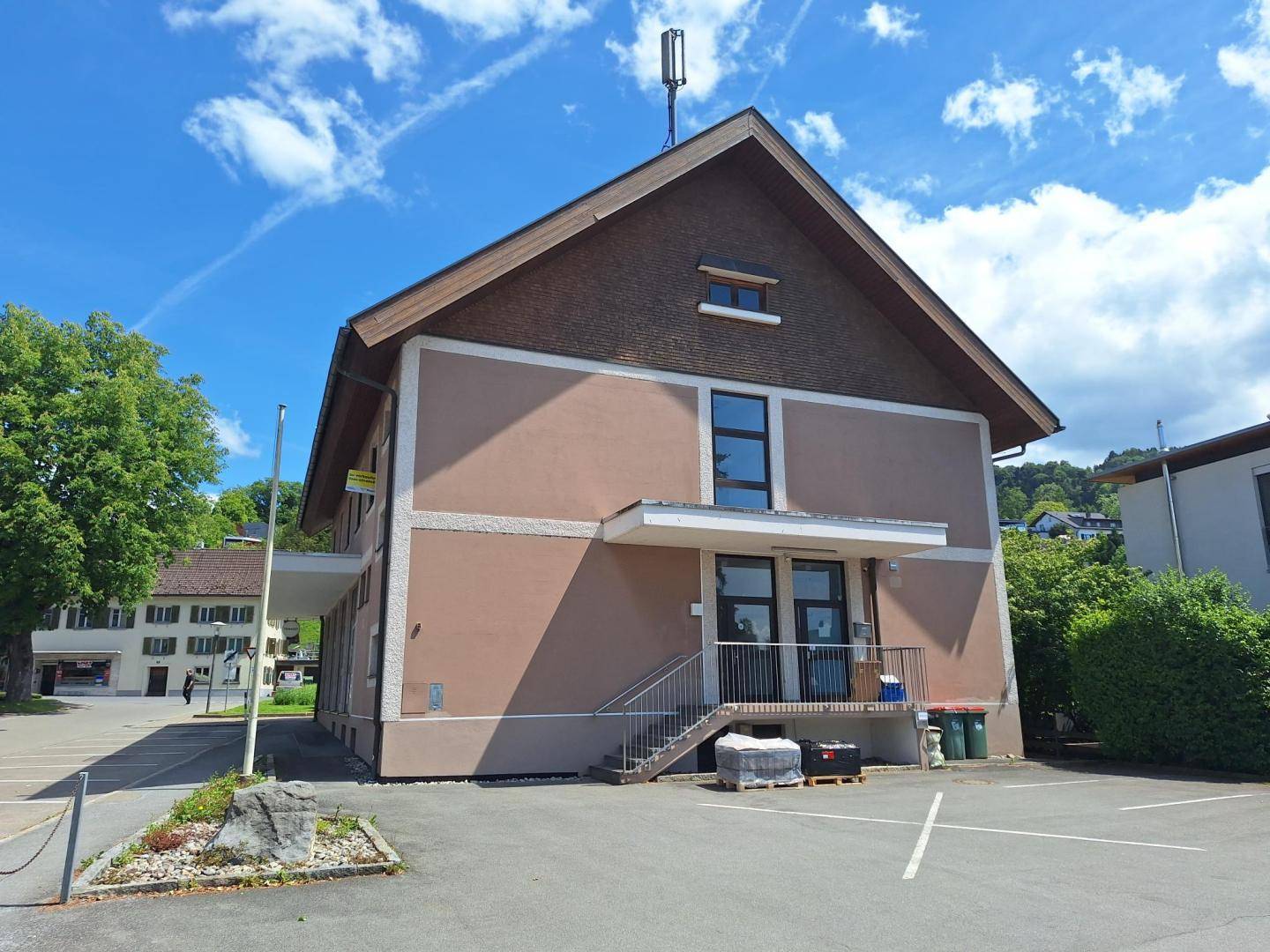 Seitenansicht des Gebäudes mit Außentreppe und angrenzendem Parkplatz unter blauem Himmel.