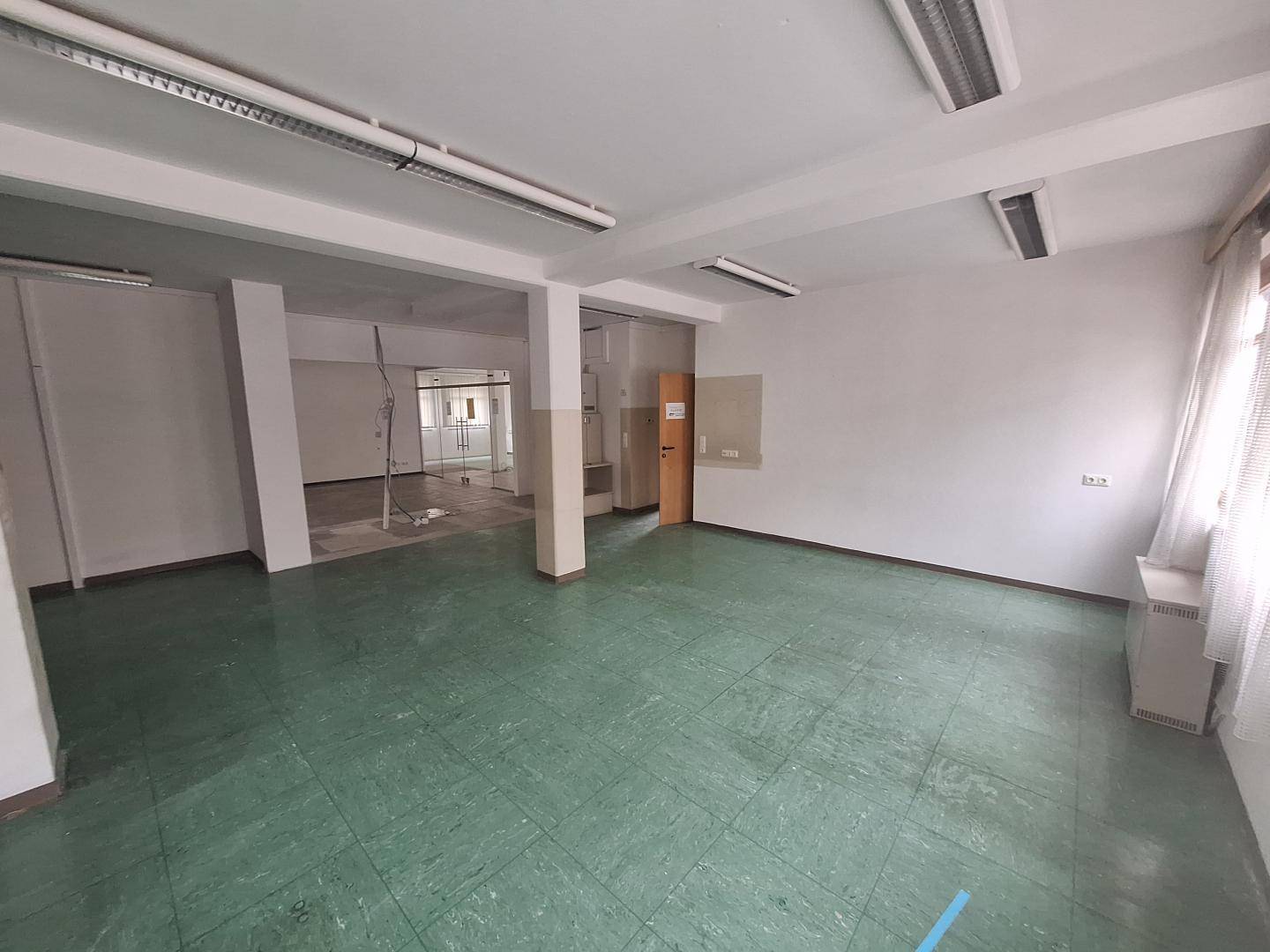 Geräumiger Gewerberaum mit grünem Fliesenboden, weißen Wänden und Deckenbeleuchtung.