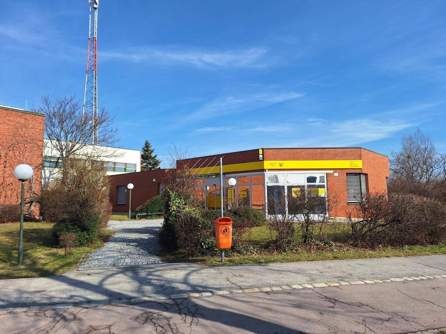Außenansicht eines Gebäudes mit gelben Akzenten und einem Mobilfunkmast im Hintergrund unter blauem Himmel.