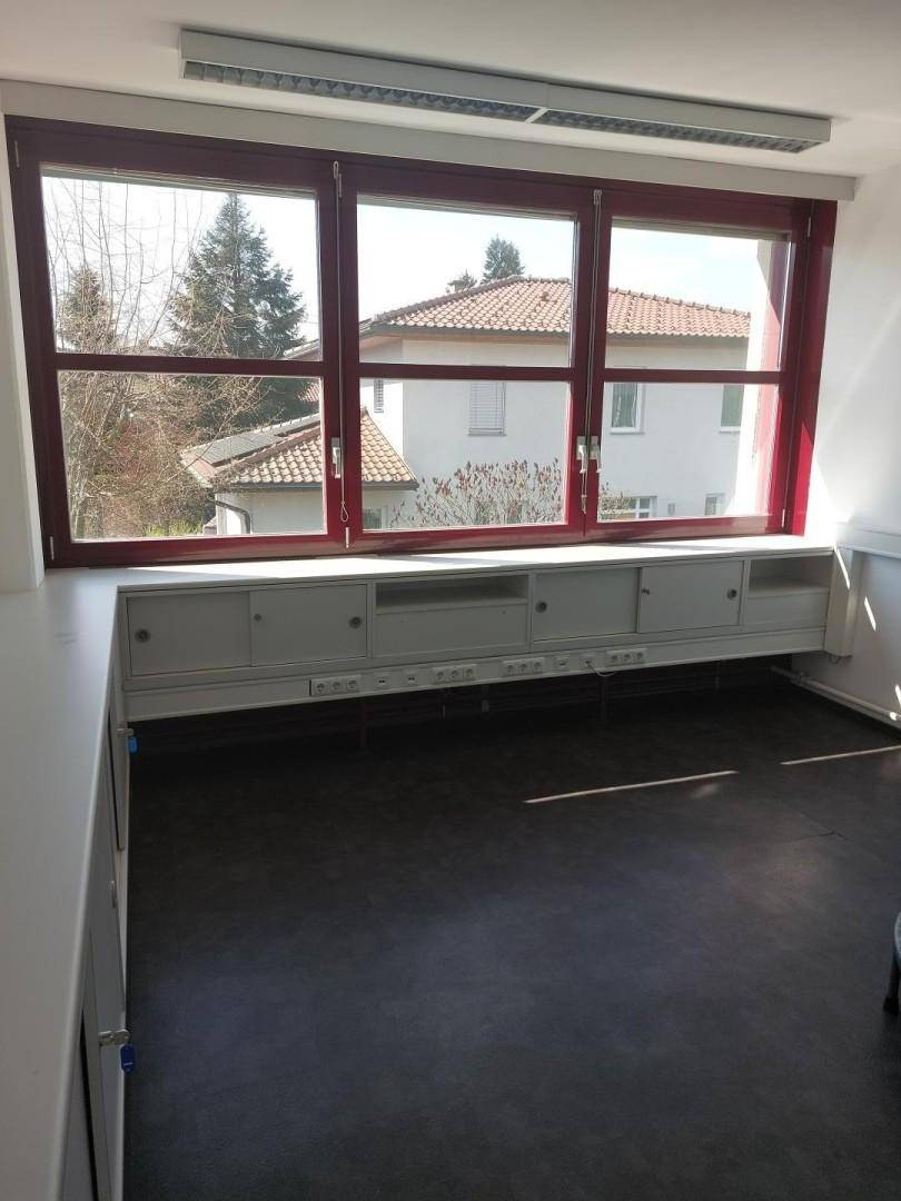 Büro mit großen Fenstern, dunklem Vinylboden und einer langen Ablagefläche mit Blick ins Grüne.