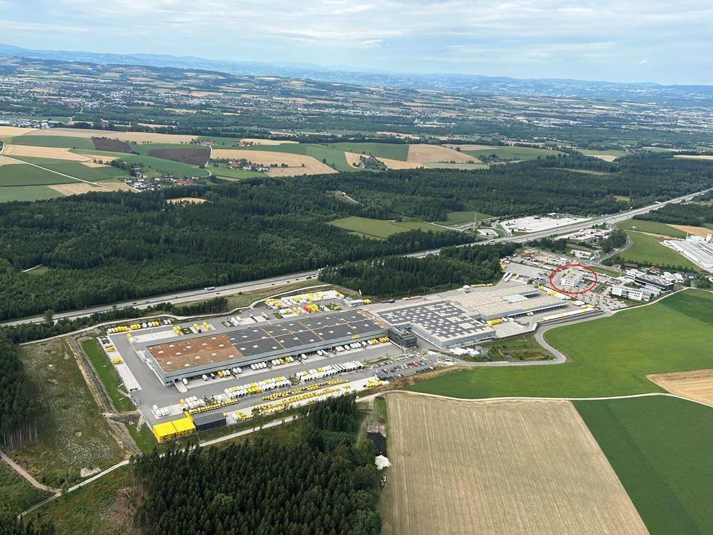 Luftaufnahme eines großen Gewerbekomplexes mit Lagerhallen, Parkplätzen und umliegender Landschaft.