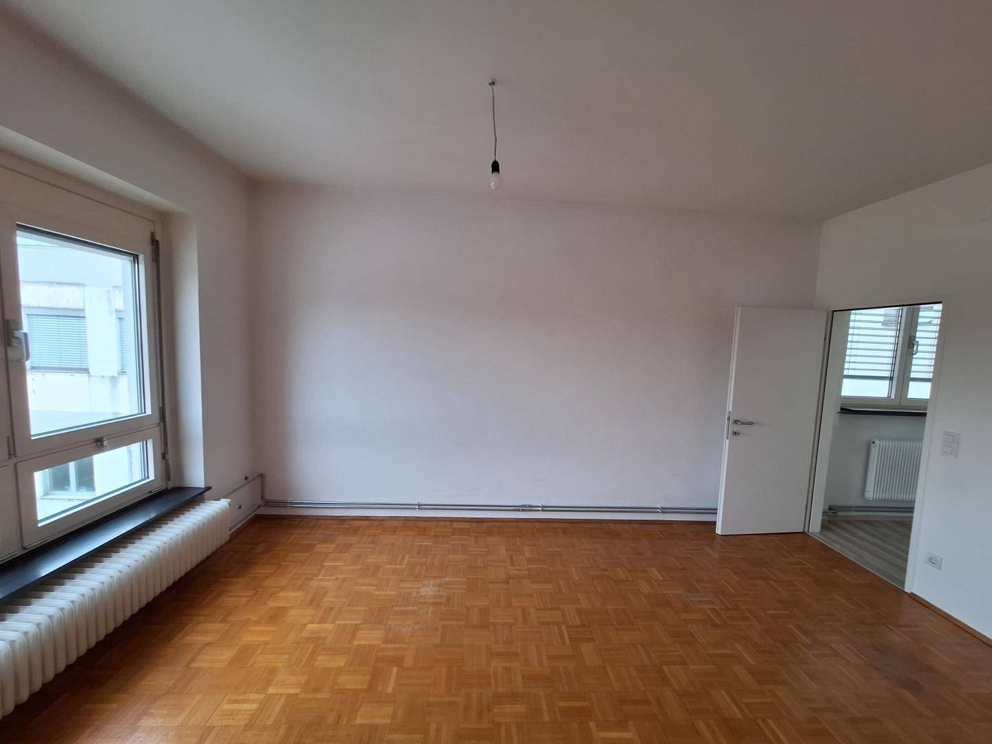 Helles Wohnzimmer mit Parkettboden und großem Fenster, das viel Licht hereinlässt.