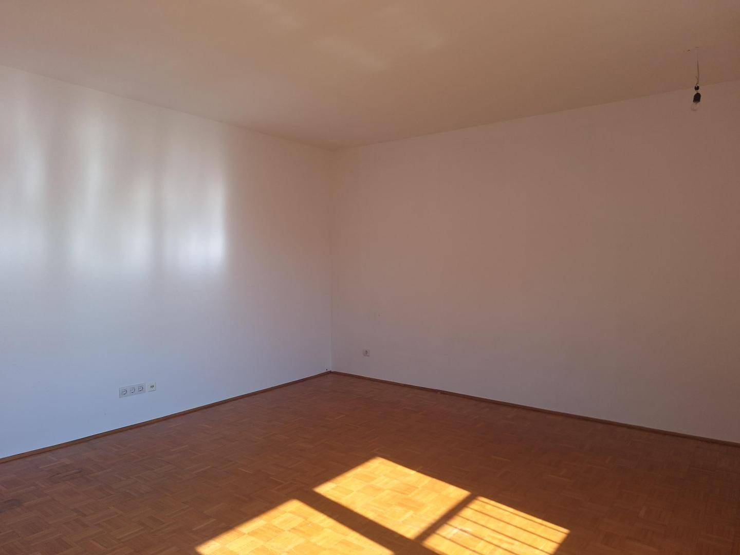Leeres Wohnzimmer mit Parkettboden und viel natürlichem Licht durch das Fenster.
