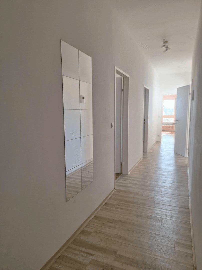 Langer, heller Flur mit modernem Laminatboden und einem Wandspiegel.
