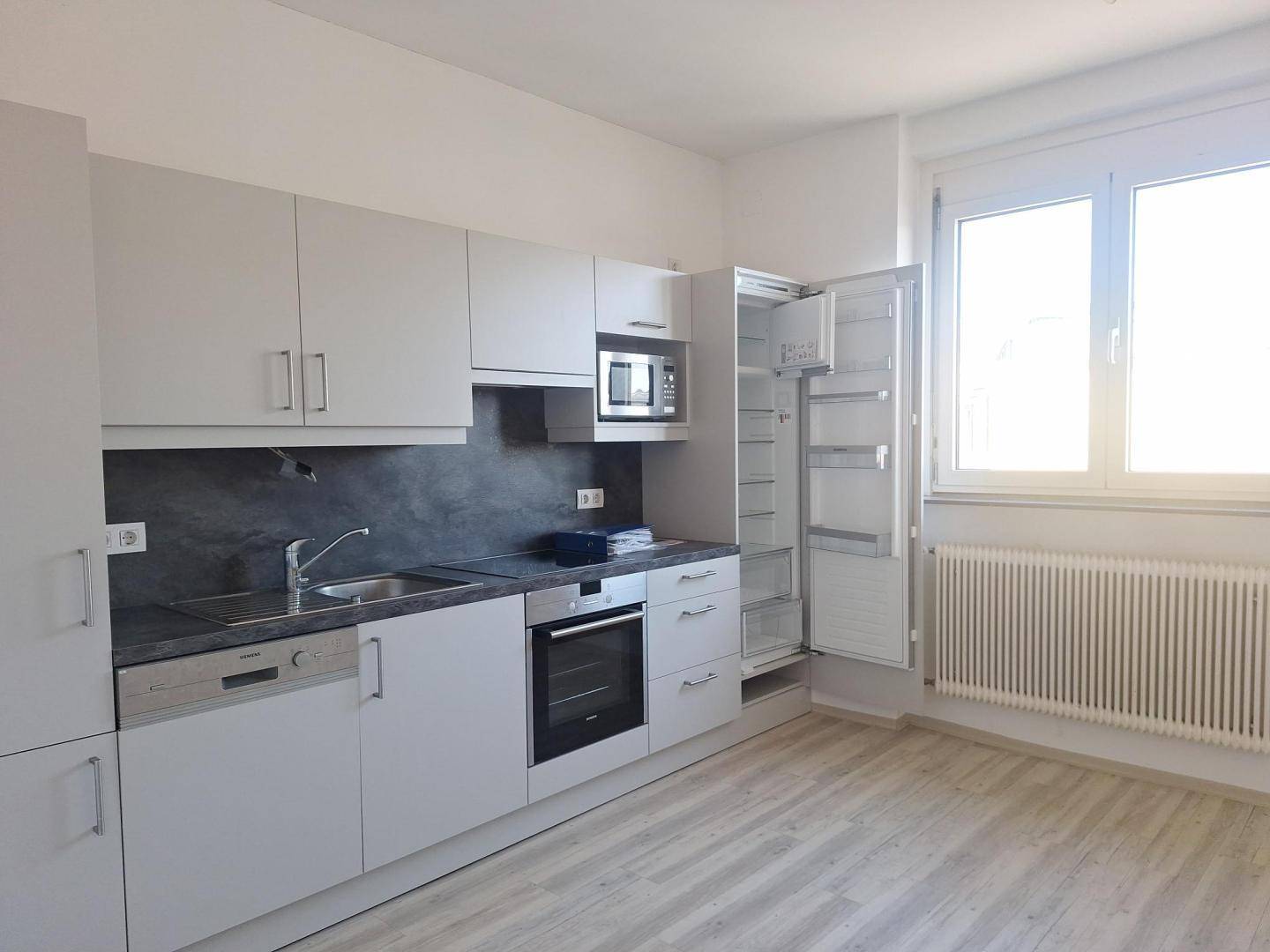 Moderne Einbauküche in Hellgrau mit integrierten Geräten und Fenster für Tageslicht.