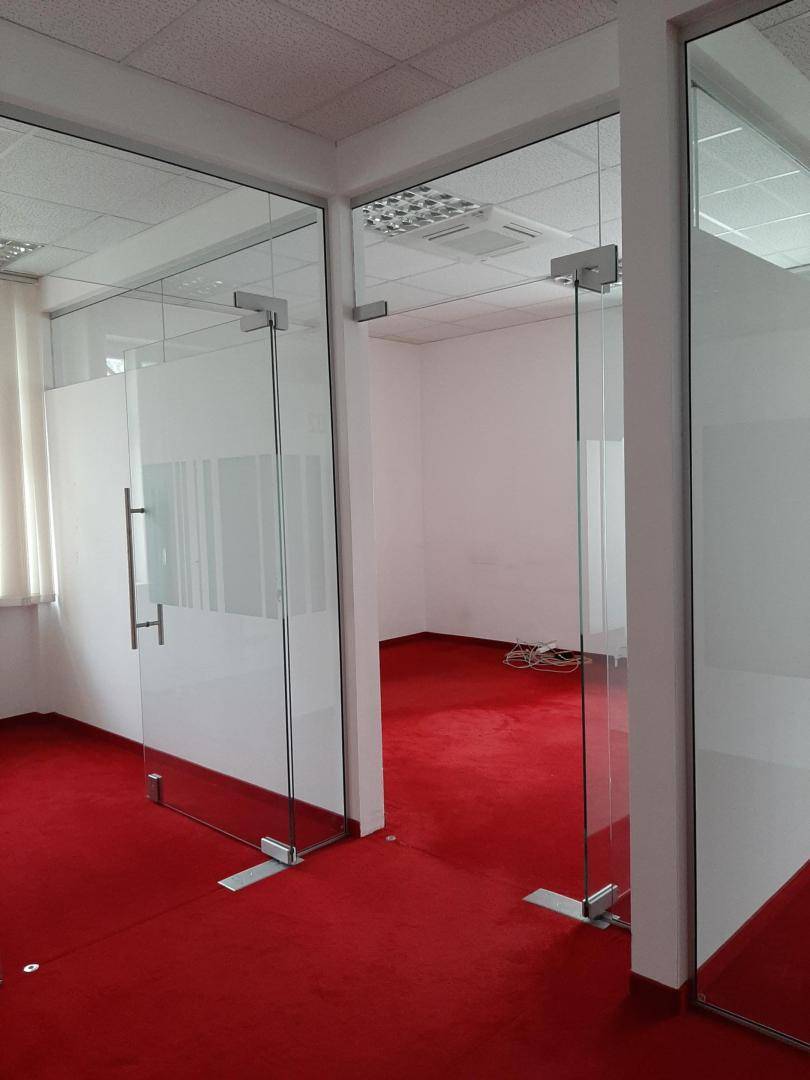 Modernes Büro mit roten Teppichböden und Glaswänden, die separate Arbeitsbereiche schaffen.