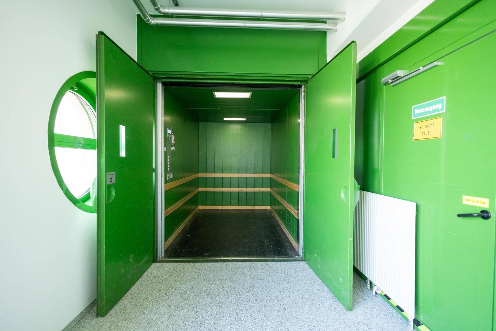 Geräumiger Lastenaufzug mit grünen Türen und Wänden, bereit für den Transport von Gütern im Gebäude.