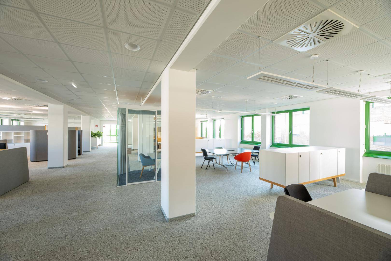 Offenes Büro mit Besprechungsbereich, ergonomischen Stühlen und effizienter Deckenlüftung.