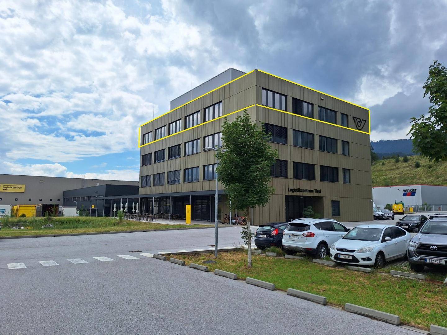 Ansicht des modernen Logistikzentrums mit brauner Fassade, umgeben von Parkplätzen und grüner Landschaft.