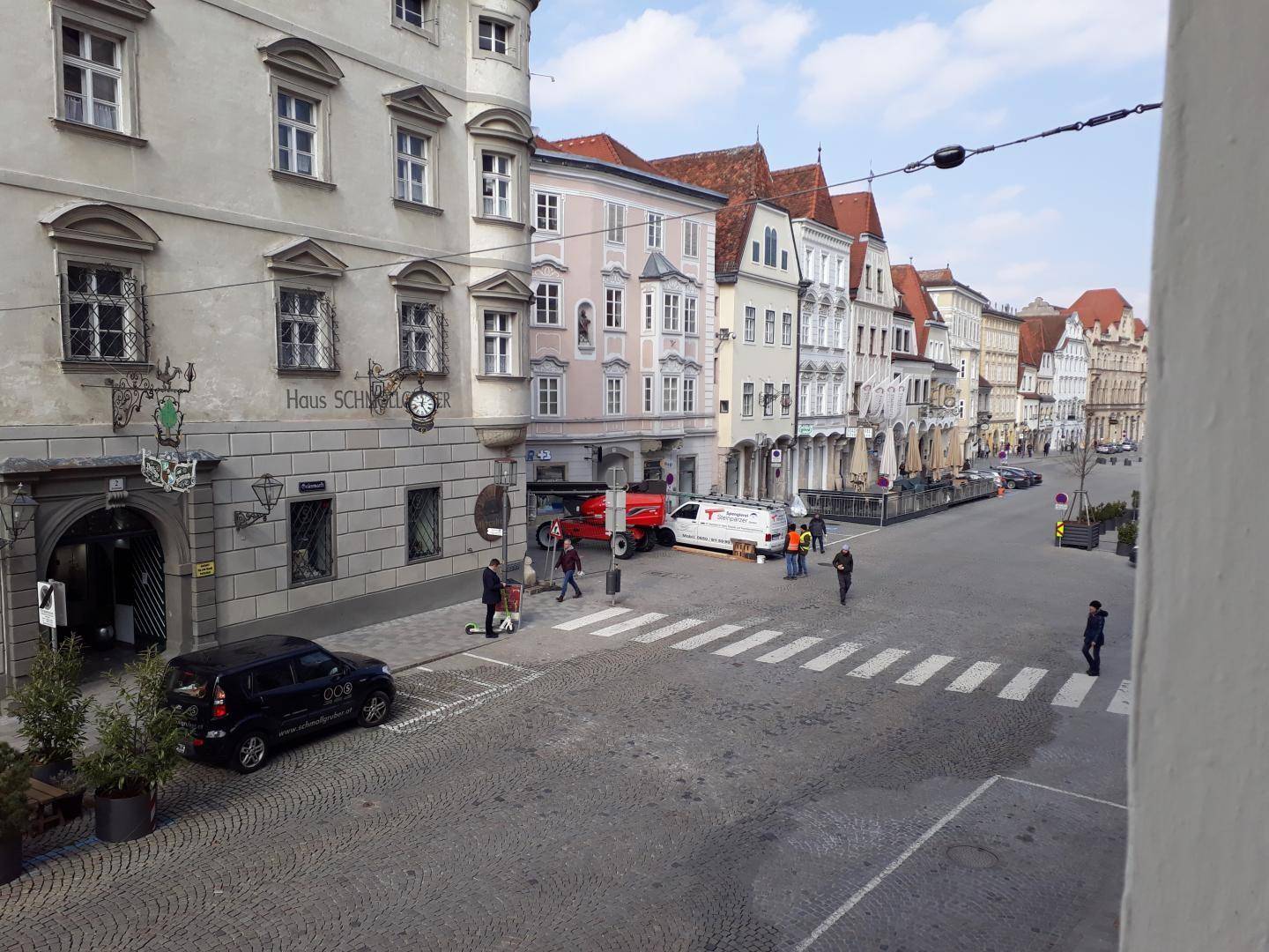 Historische Altstadtgasse mit Kopfsteinpflaster, traditionellen Gebäuden und Passanten an einem sonnigen Tag.