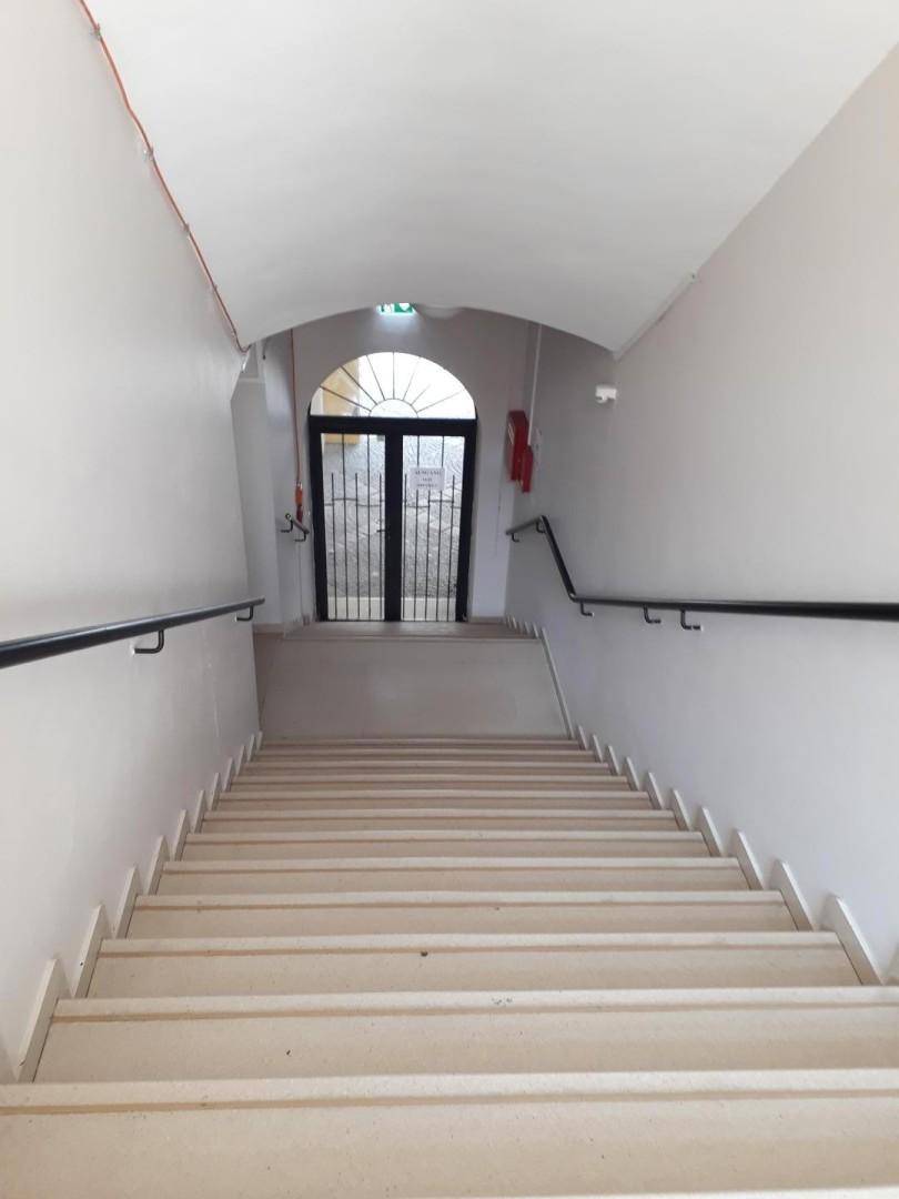 Treppenhaus mit Handläufen und einer gewölbten Decke, die zu einer Gittertür führt.