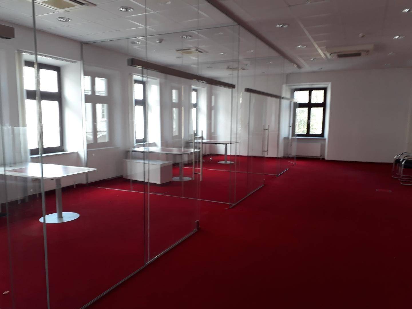Heller Büroraum mit rotem Teppich, modernen Glaswänden und großen Fenstern mit Blick nach draußen.