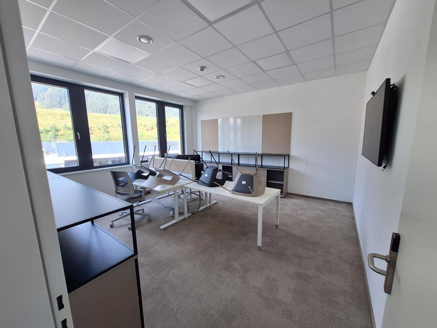 Besprechungsraum mit Teppichboden, großen Fenstern und flexiblen Tischen, bereit für Meetings.