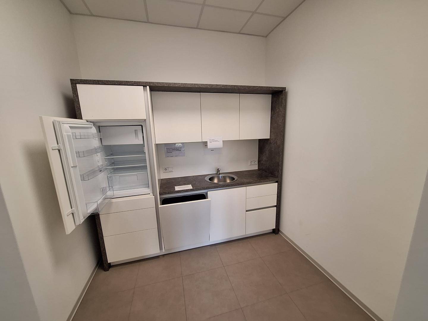 Kleine, kompakte Küchenzeile mit integriertem Kühlschrank und Spüle in einem hellen Raum.