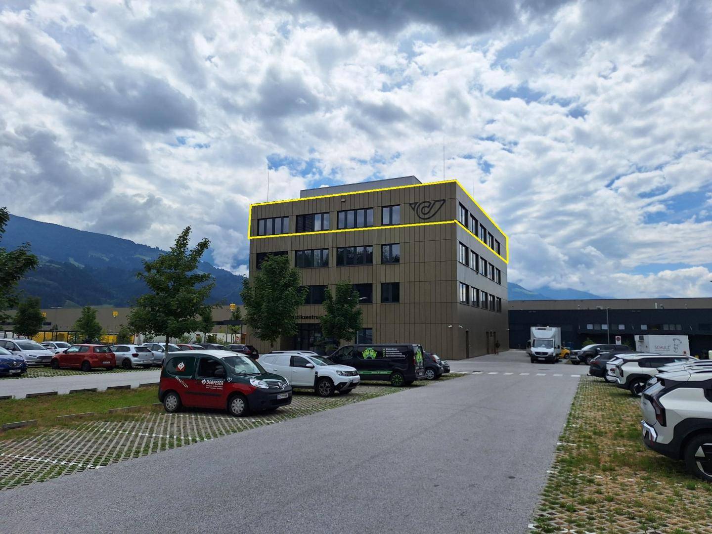 Modernes Bürogebäude mit markanter Fassade und großem Parkplatzbereich unter bewölktem Himmel.