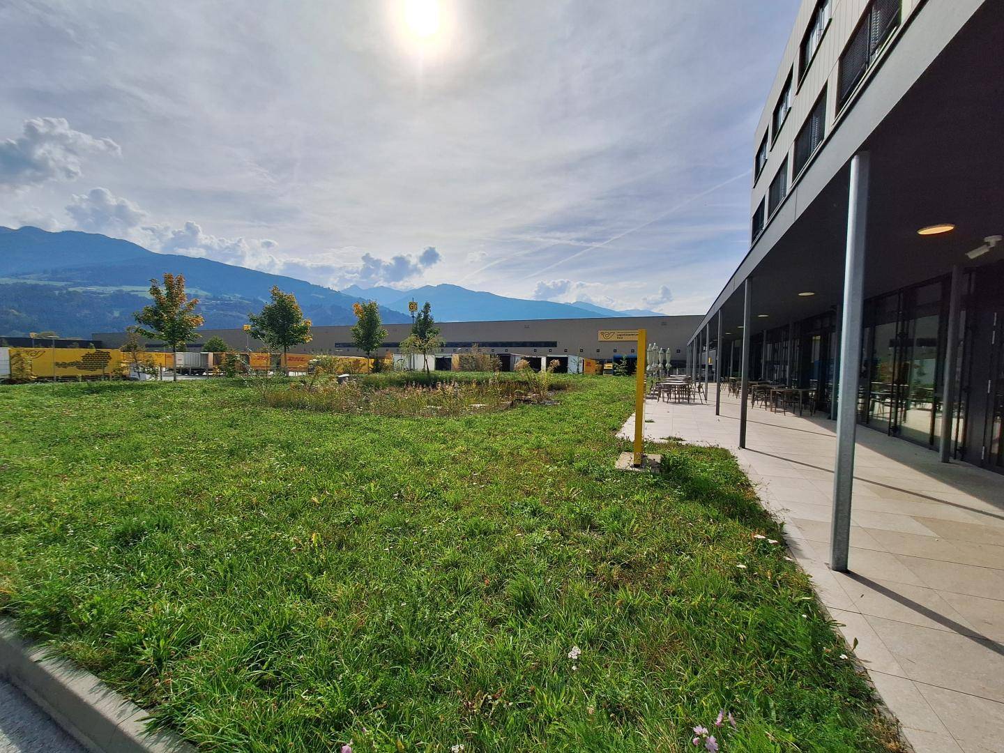 Grüne Rasenfläche vor dem Gebäude mit Blick auf die Berge und eine sonnige Terrasse.