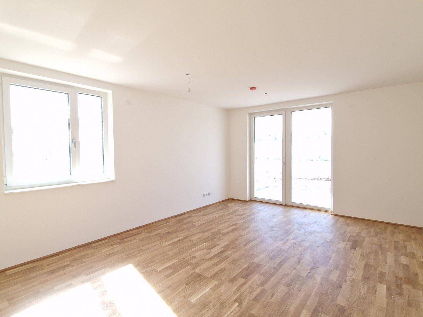 Lichtdurchfluteter Wohnbereich mit Holzboden und Zugang zu einem Außenbereich.