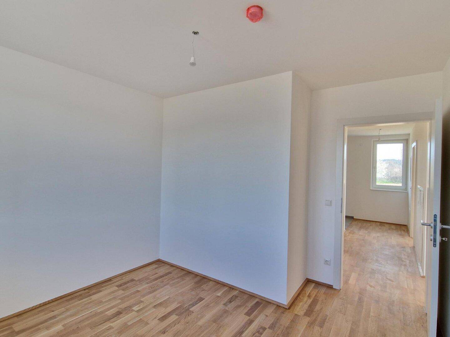 Helles Schlafzimmer mit Parkettboden und Blick in einen weiteren Raum.