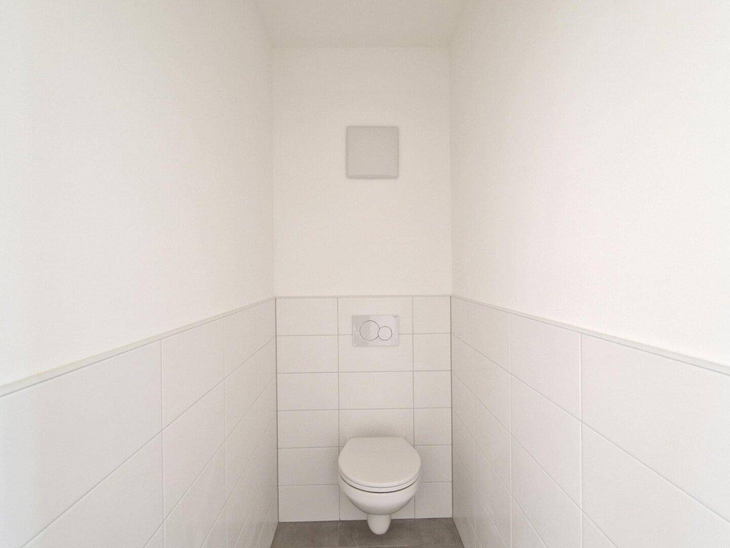 Separate Toilette mit Wand-WC und weißen Fliesen.