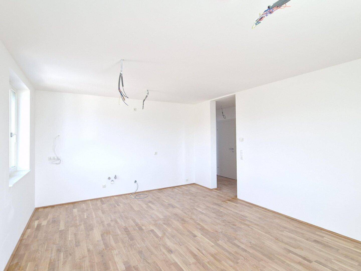 Geräumiger Wohnbereich mit Parkettboden und Anschlüssen für eine zukünftige Küche.