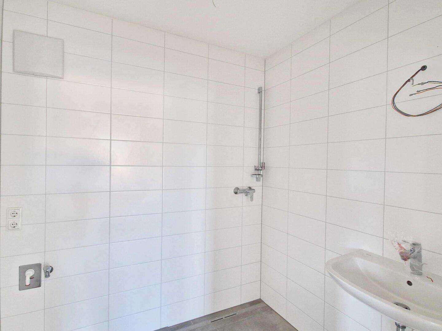 Modern geflieste Duschkabine mit Waschbecken und Wandarmatur.