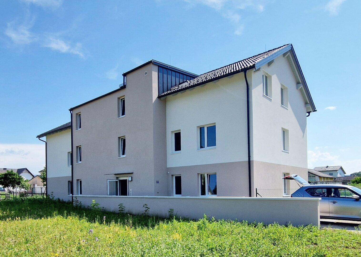 Rückansicht eines modernen Mehrfamilienhauses mit schlichter Fassade und Satteldach unter blauem Himmel.