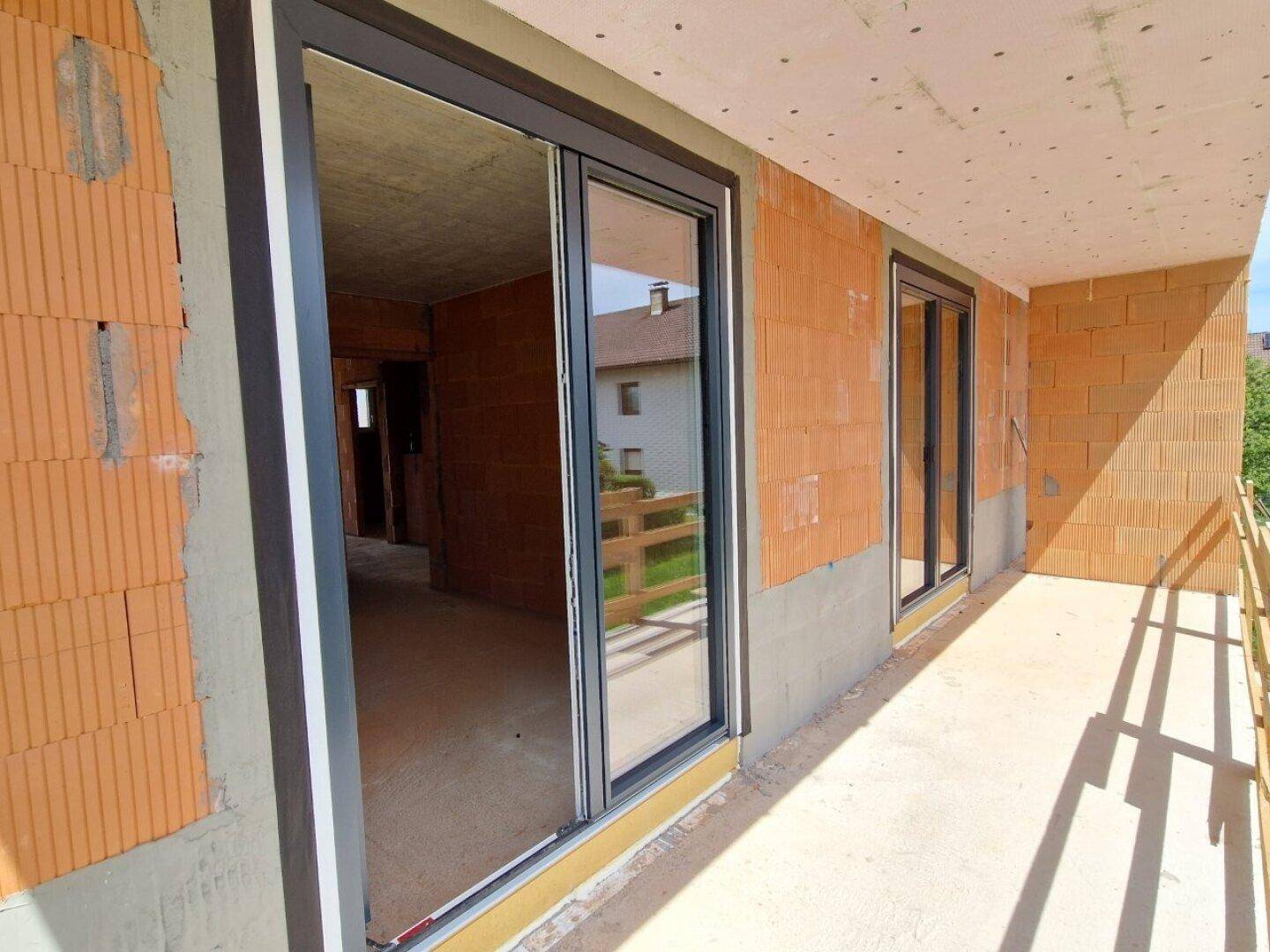 Balkon im Rohbau mit Schiebetüren zu den Innenräumen und Blick auf die Umgebung.