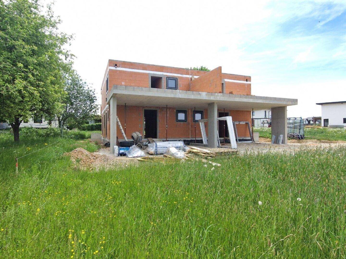 Vorderansicht des Neubaus mit Betonüberdachung und Ziegelwänden im Rohbau.